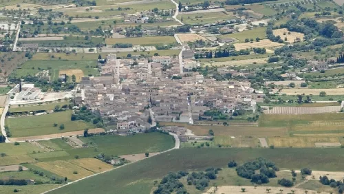 Luftaufnahme eines kleinen Dorfes mit vielen Gebäuden und Feldern im Umland.
