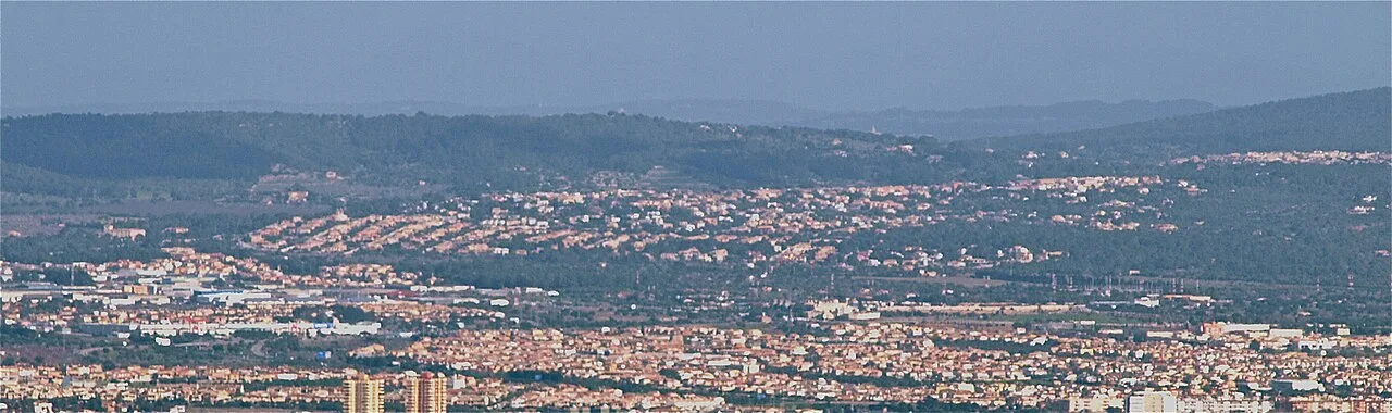 Stadtansicht mit urbanen Gebieten und entfernten Hügeln im Hintergrund.