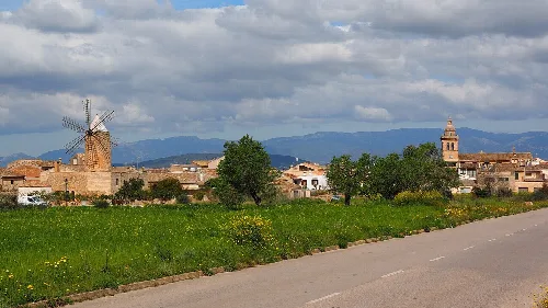Dorfansicht mit Windmühle, Kirchturm und Wolken im Himmel.