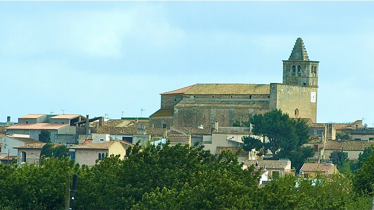 Stadtbild von Búger mit Kirche und Häusern, umgeben von Bäumen.