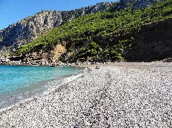 Sandstrand mit grünen Hügeln und Klippen im Hintergrund.