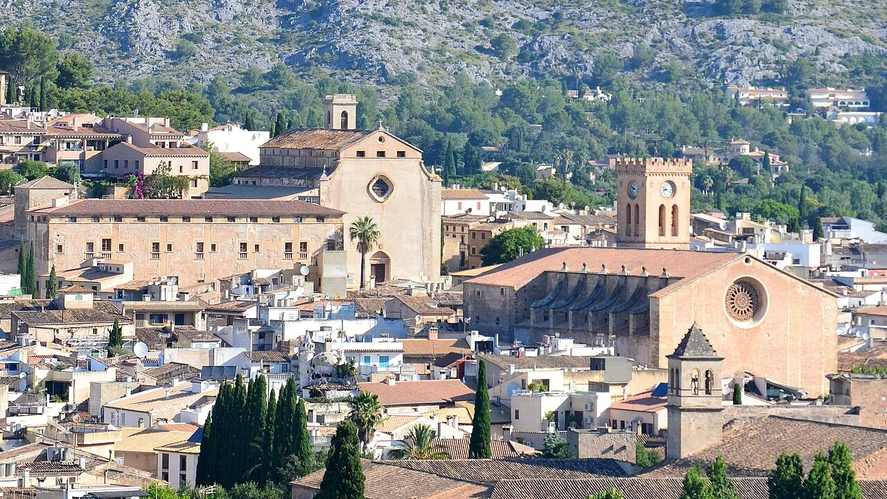 Stadtansicht von Pollença mit Kirchen und Bergen im Hintergrund.