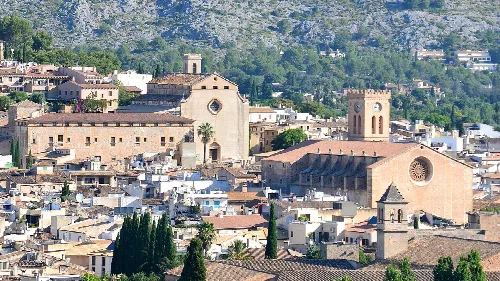 Stadtansicht von Pollença mit Kirchen und Bergen im Hintergrund.